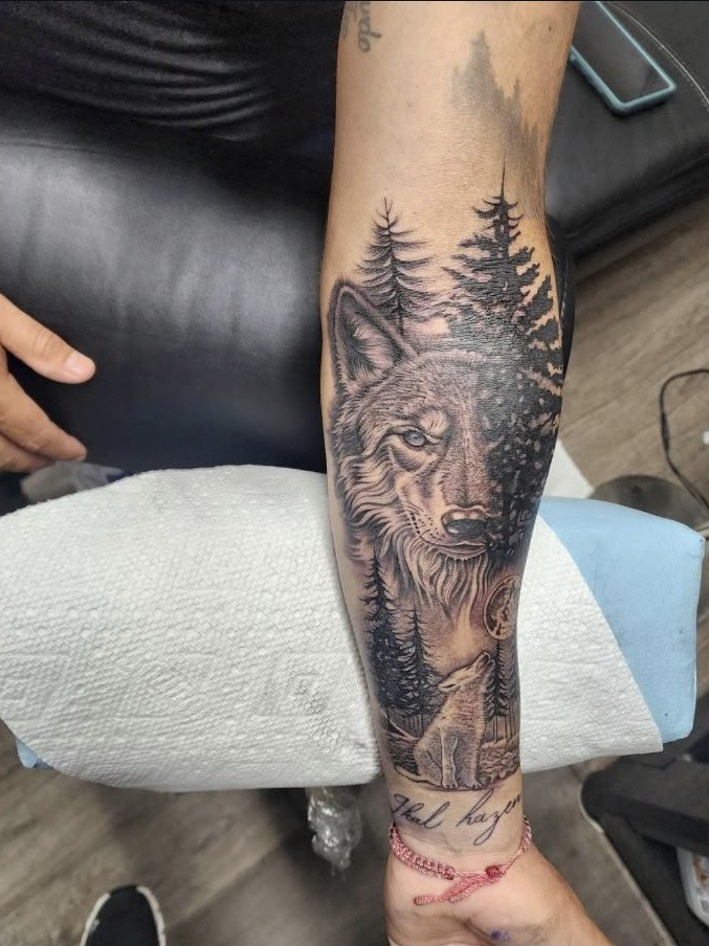 Black and grey wolf and pine forest forearm tattoo by Miguel